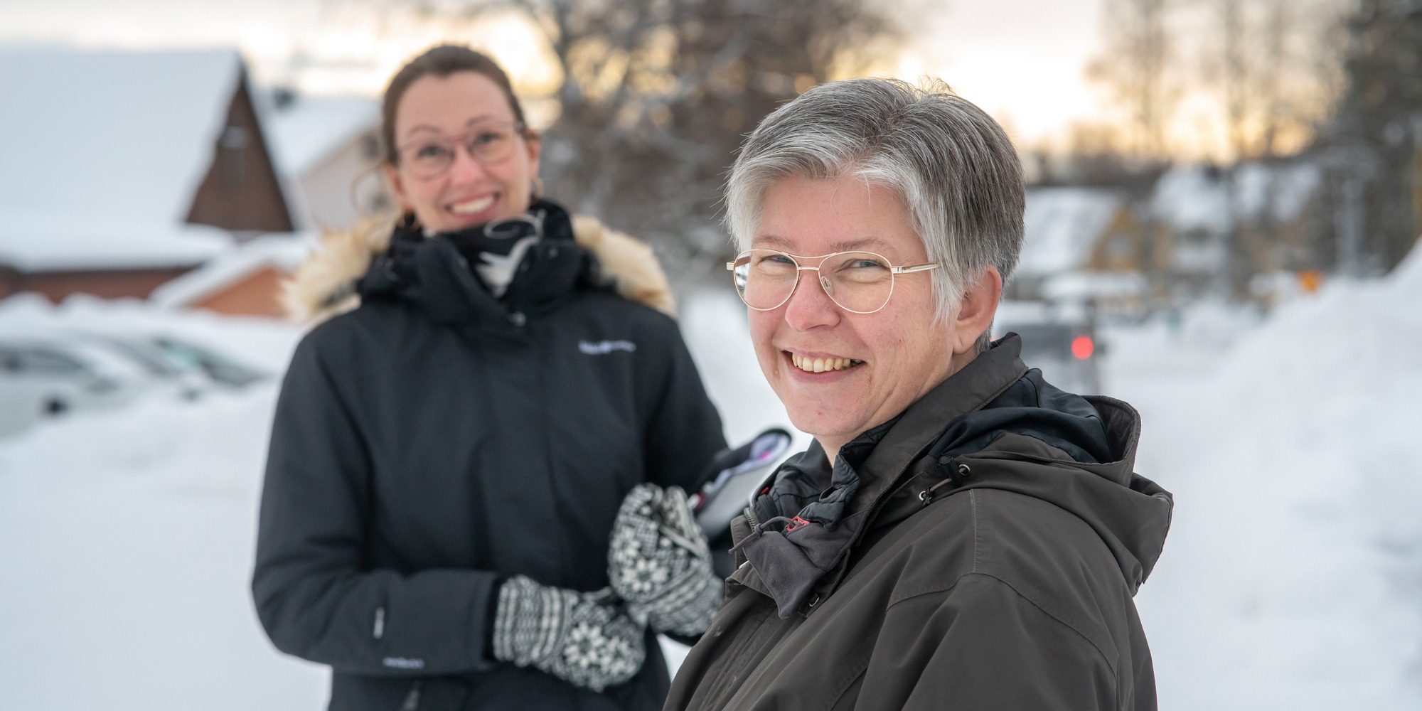 Tv&aring; leende kvinnor st&aring;r ute i sn&ouml;landskap.
